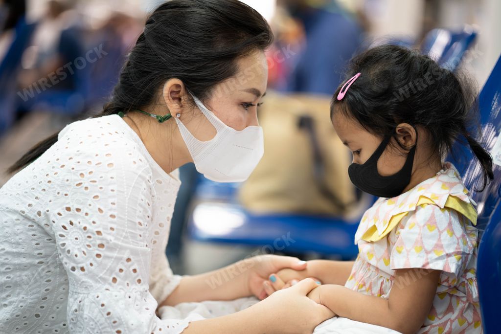 A young mother and daughter wearing a protective face mask waiting for departure.