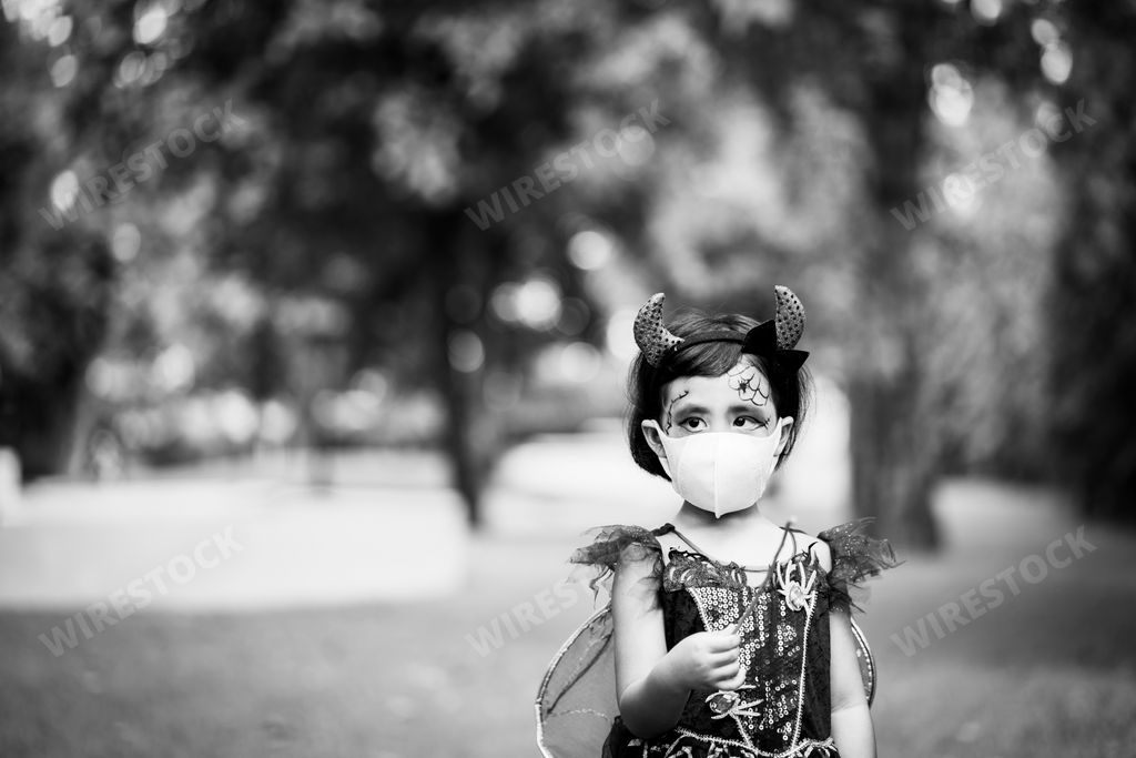 A grayscale shot of a Southeast Asian girl wearing her costume and also a facemask on Halloween, outdoors