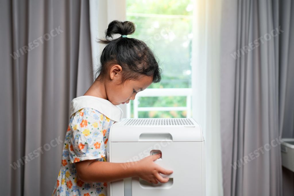 A cute five-year-old Asian girl breathing fresh air from an air washer