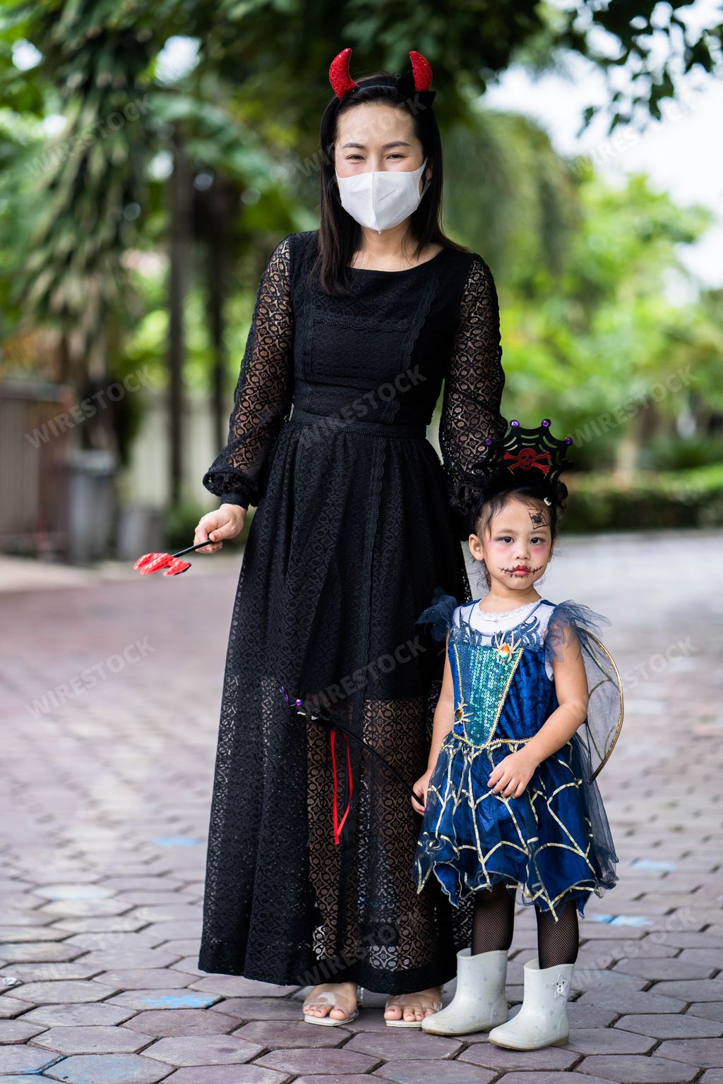 A vertical shot of a Thai mother and her little girl in Halloween costumes standing outdoors