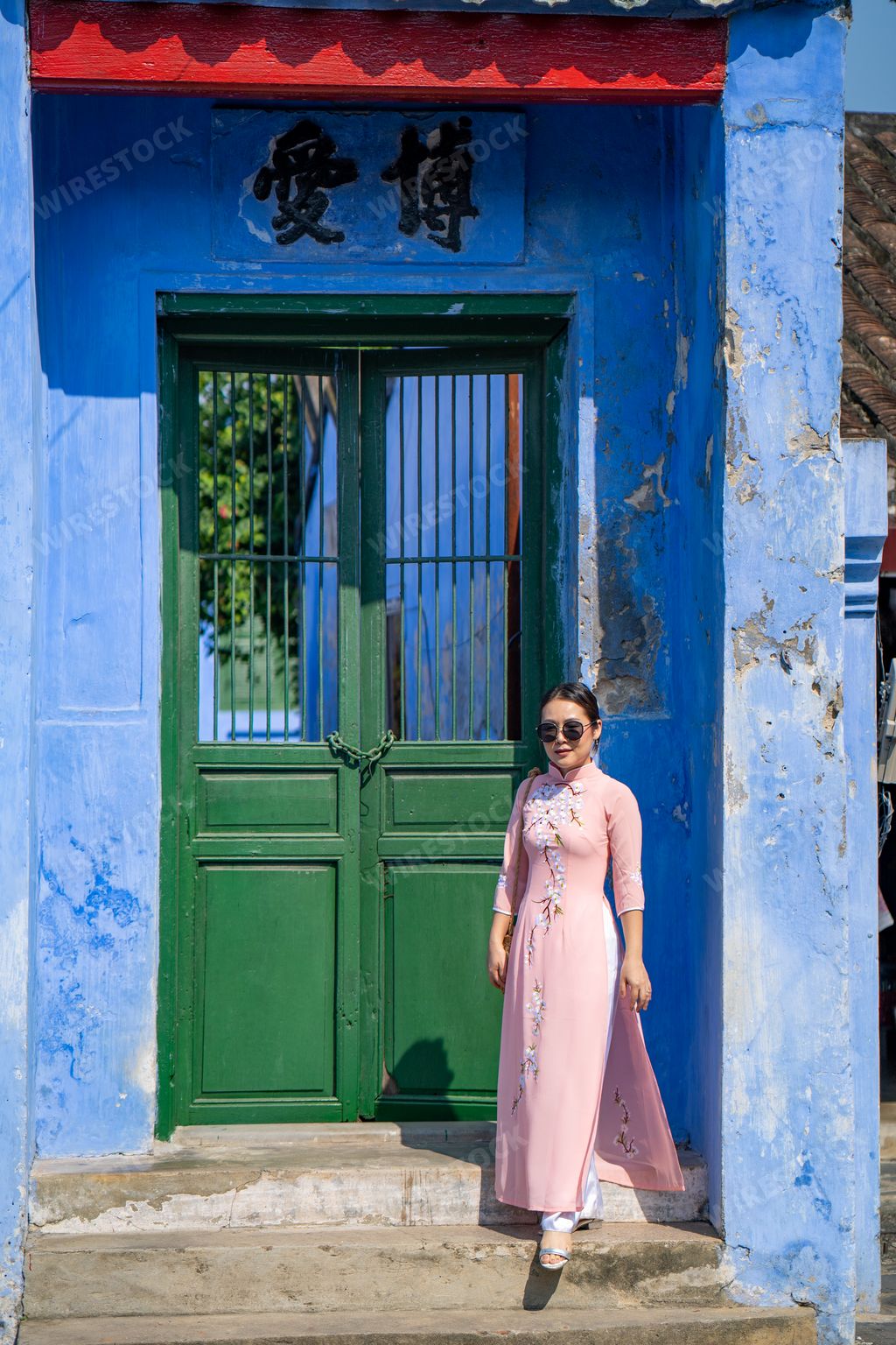 A vertical shot of a beautiful Southeast Asian young female standing near blue walls in front of a green door