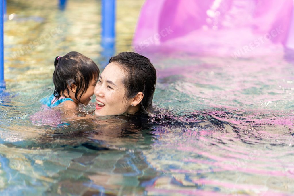 A young Thai mother swimming in a pool with her little daughter