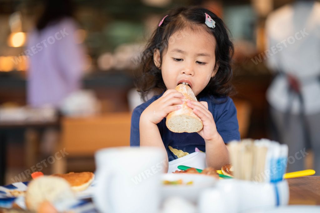 A closeup of a little girl eating a loaf of bread.
