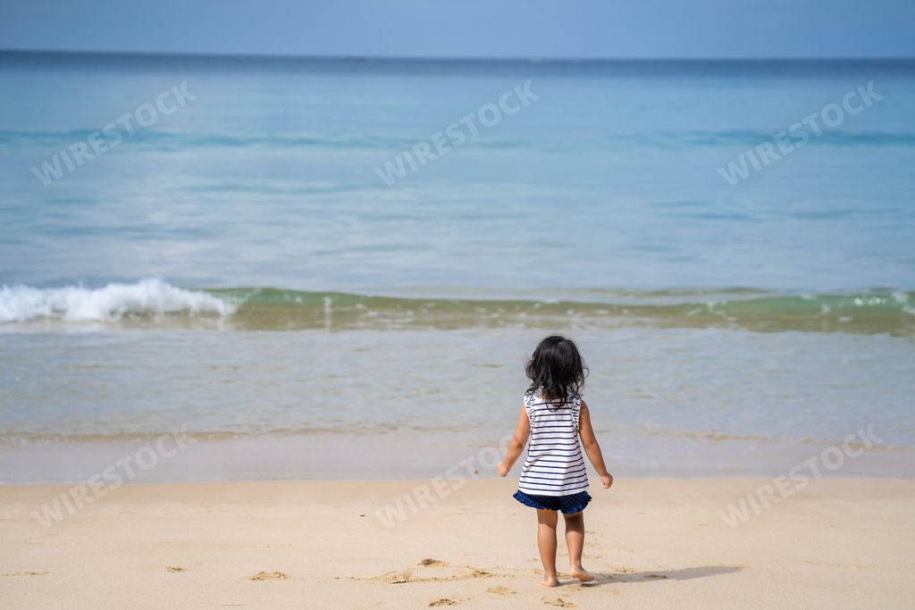 A back view of a little Thai girl standing on the coast of the sea