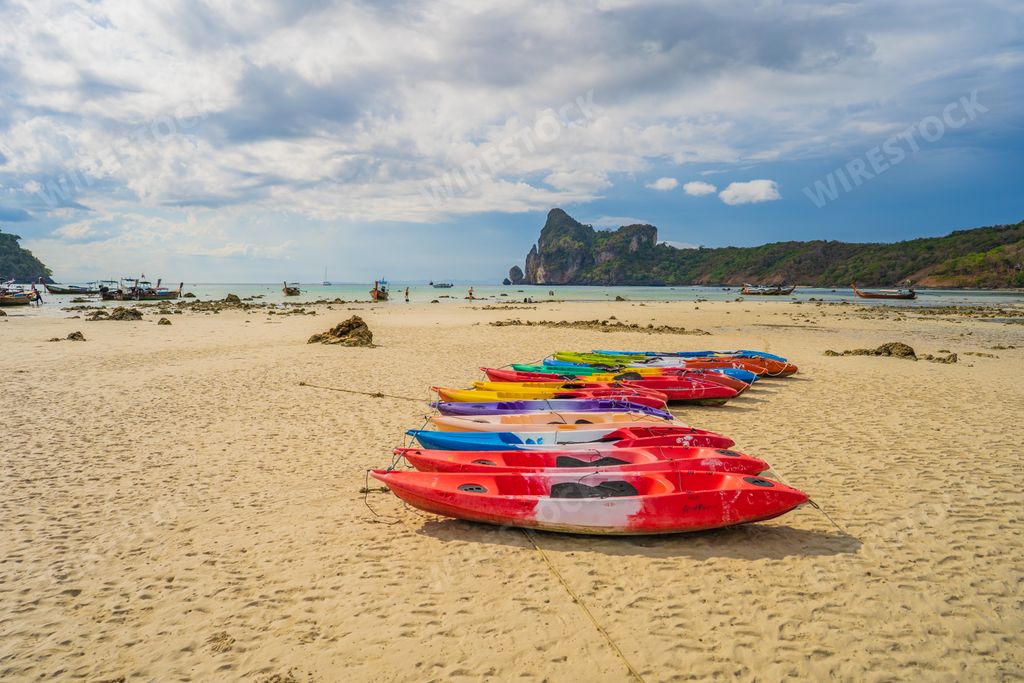 A closeup of a row of colorful kayaks at white sand beach resort