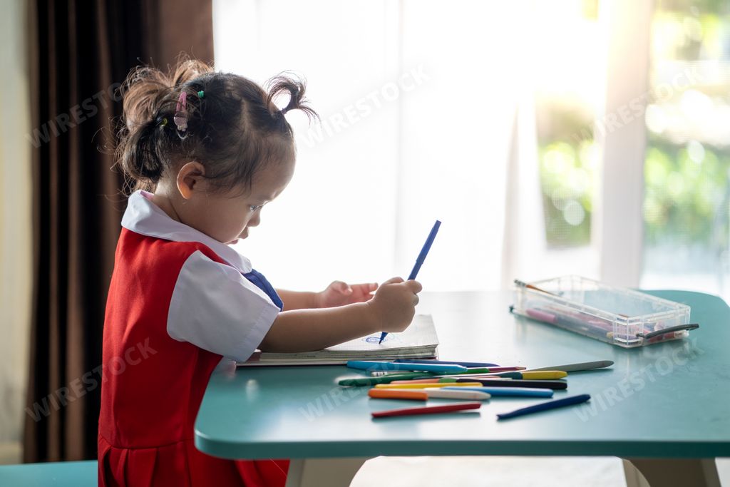 A little Thai girl drawing with a blue marker