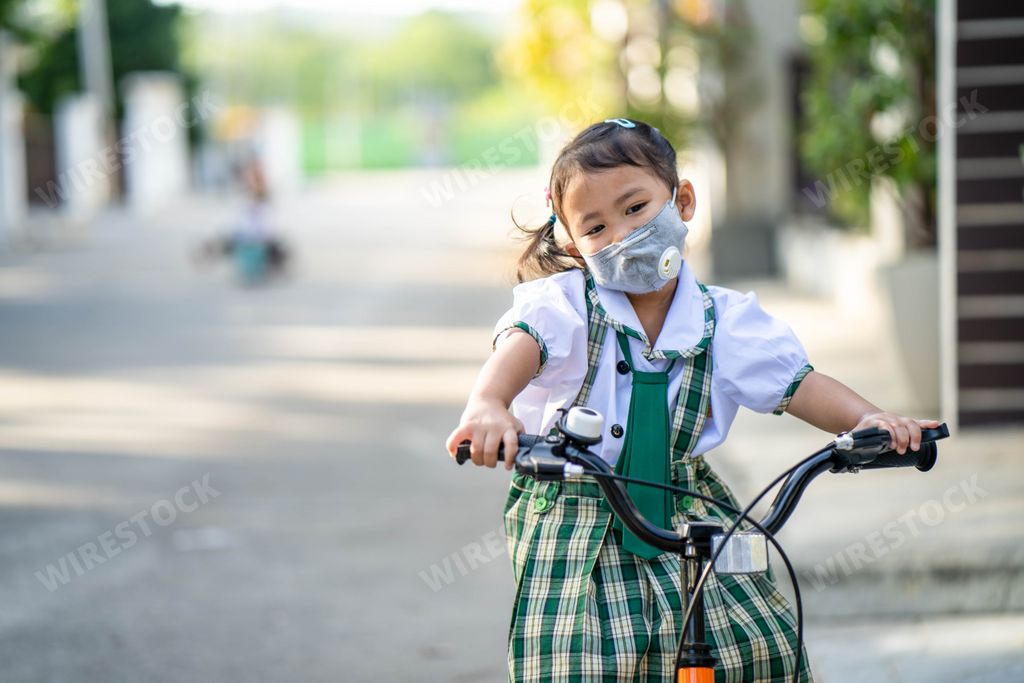 A cute little Thai girl in a school uniform and a face mask riding a bike