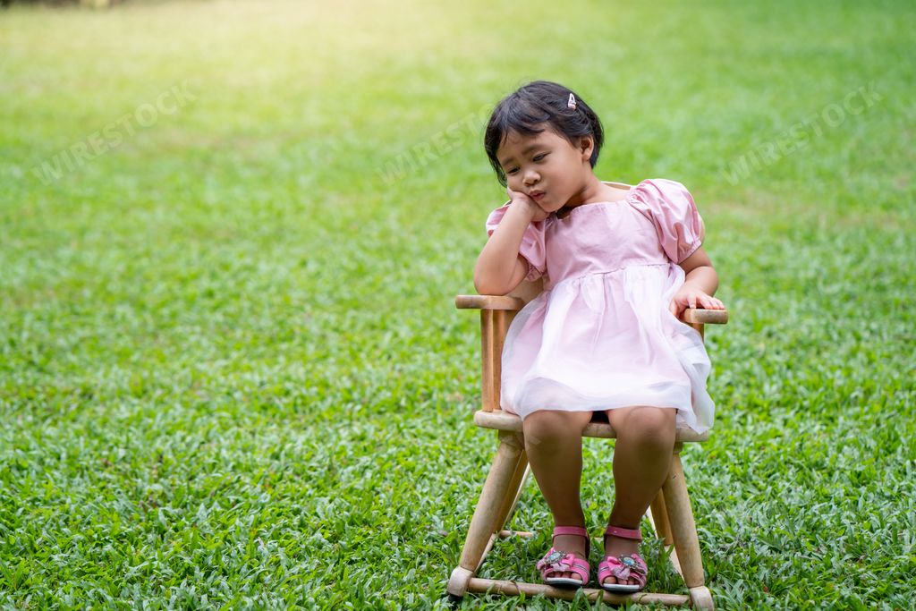 A tired little Asian girl sitting on a chair in the green grass