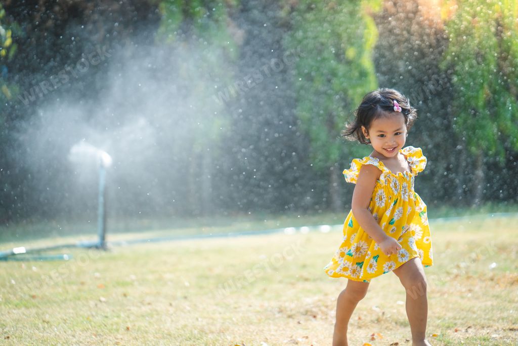 An adorable little Asian girl in a yellow dress playing in the garden with splashing water