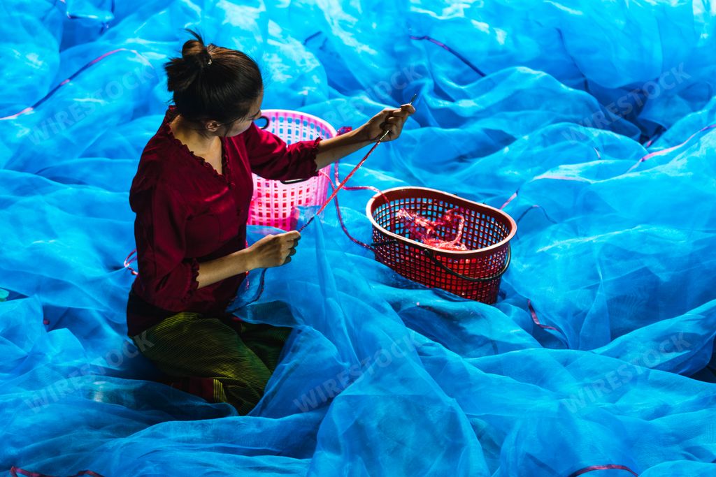 A Southeast Asian women is sewing the fishnet at the Fishing village