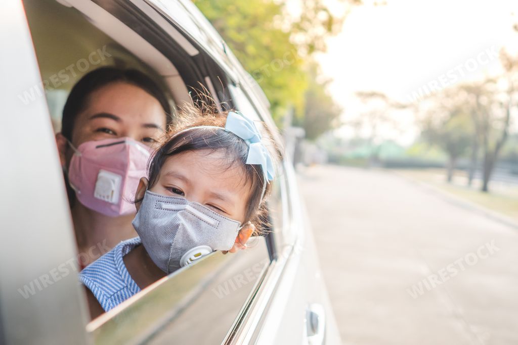 An Asian mother and daughter wearing face mask seen through a car window