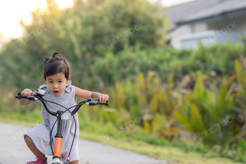 A small Asian female child riding a bicycle in a park