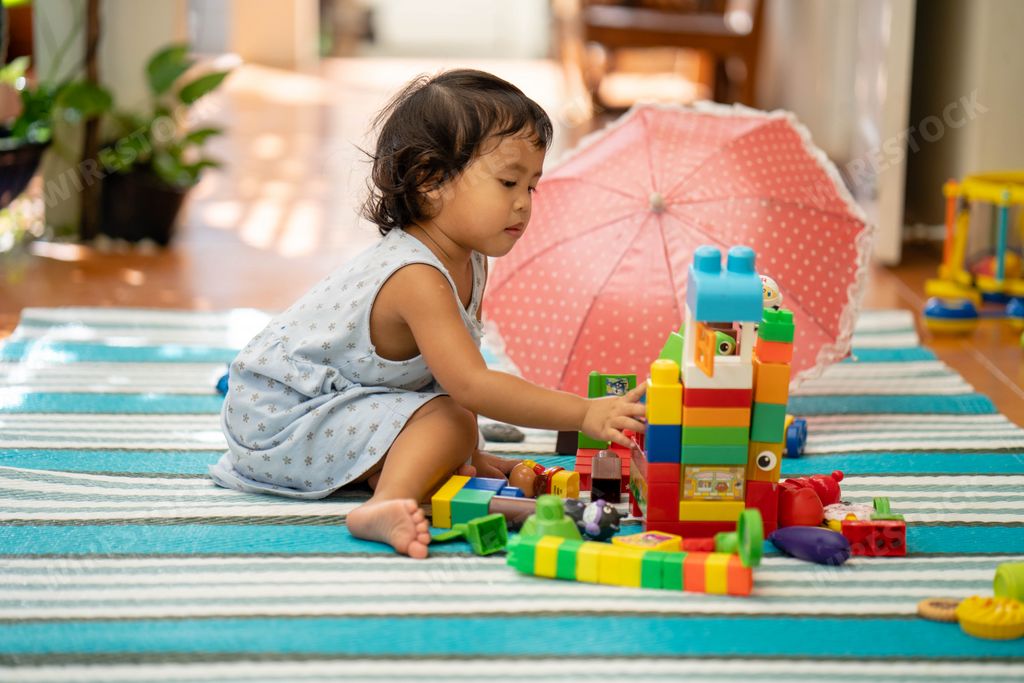 A closeup of a little girl playing with colorful construction toys on the floor.