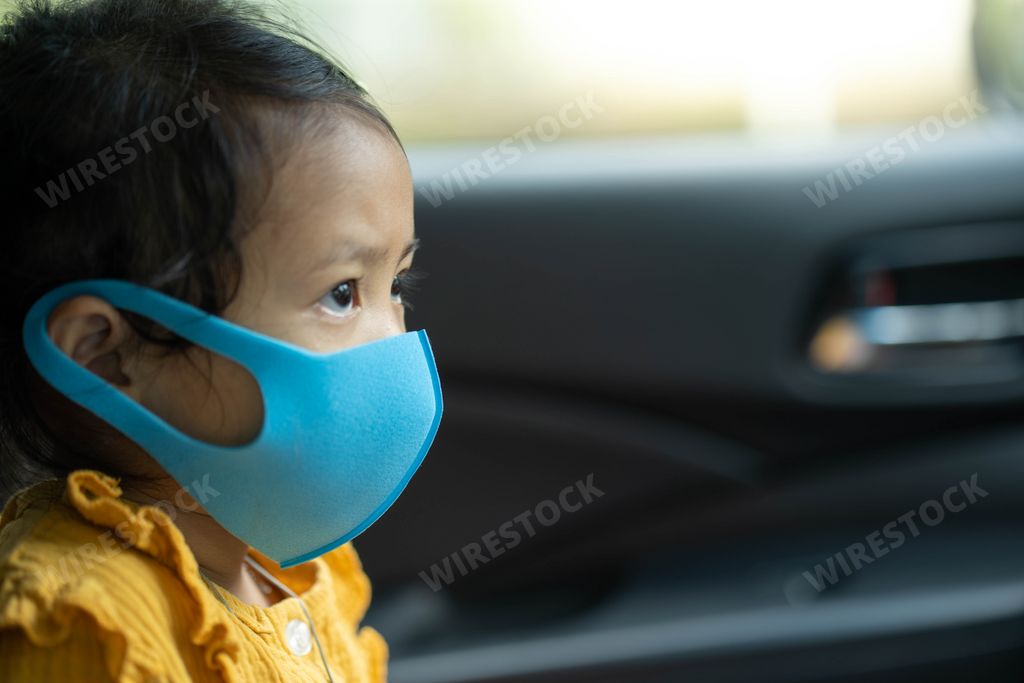 An adorable little Thai girl sitting in a car wearing a protective face mask