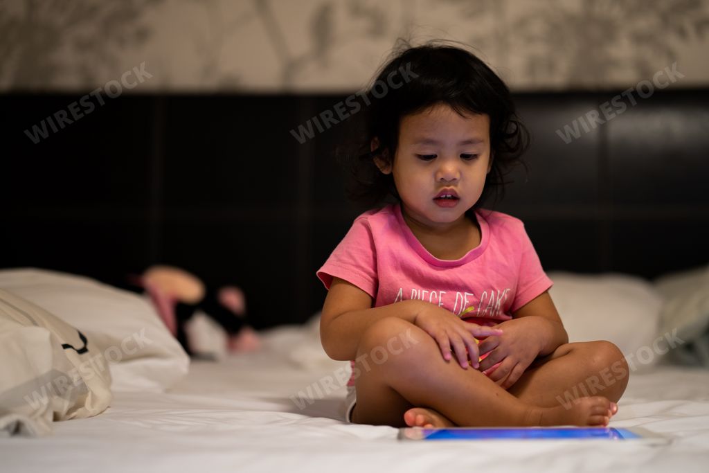 A shallow focus shot of a little Thai girl using a digital tablet on a bed