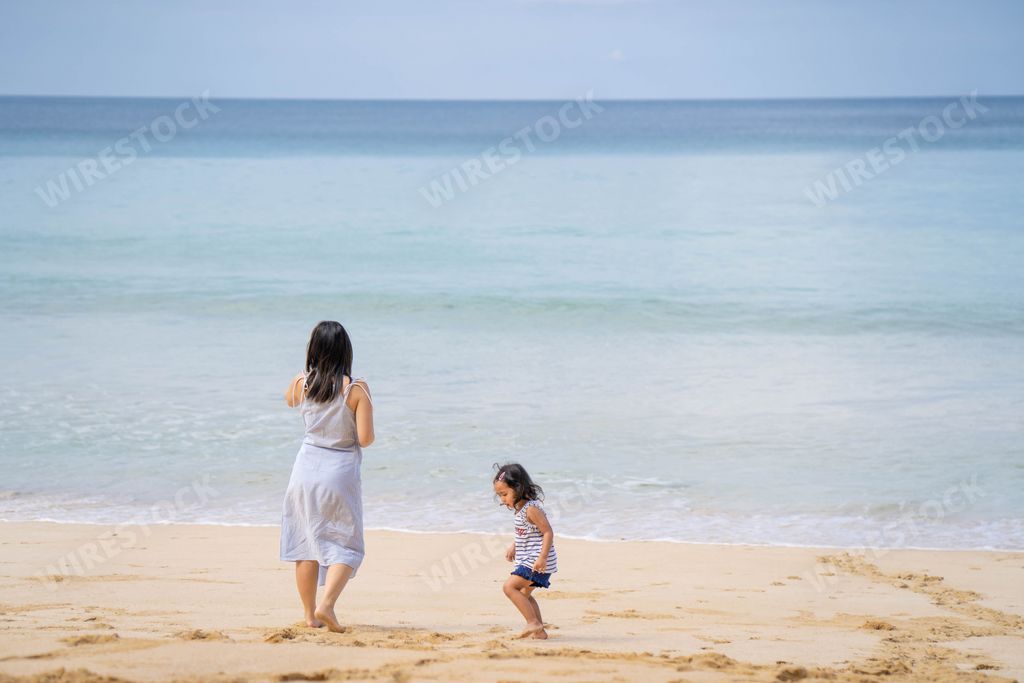 A young mother and daughter standing at seashore against blue sky