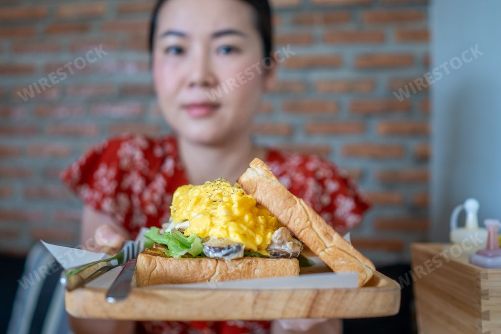 A beautiful Thai woman holding tuna egg sandwich at a restaurant