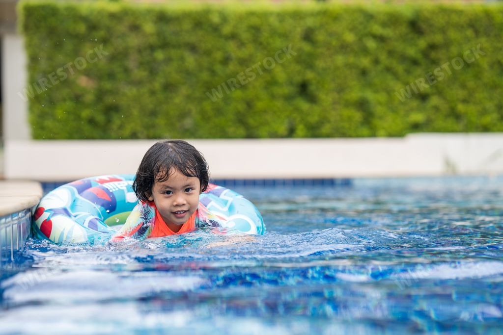 A shallow focus of a young Southeast Asian girl swimming at a pool using a swim tube