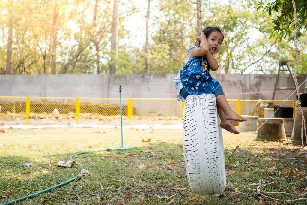 A little Thai girl hanging on a swinging car tire at a playground