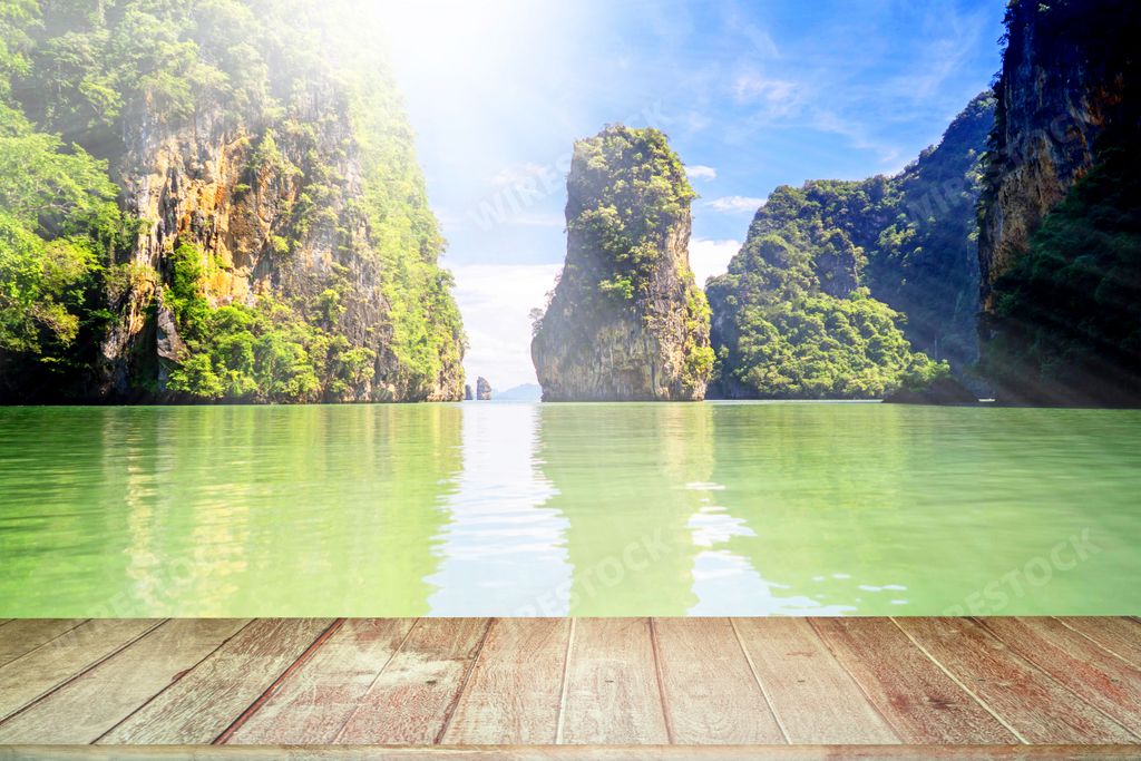 A wooden dock against a lake with green mountains in sunlight