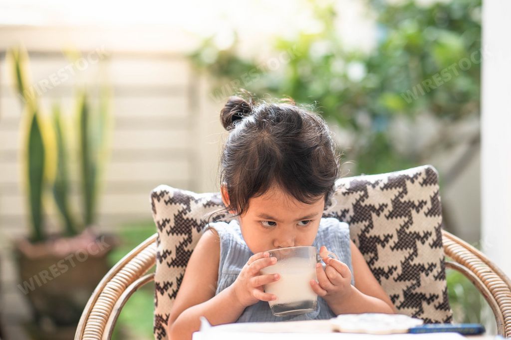 An adorable Asian female child drinking a glass of milk near an outdoor table