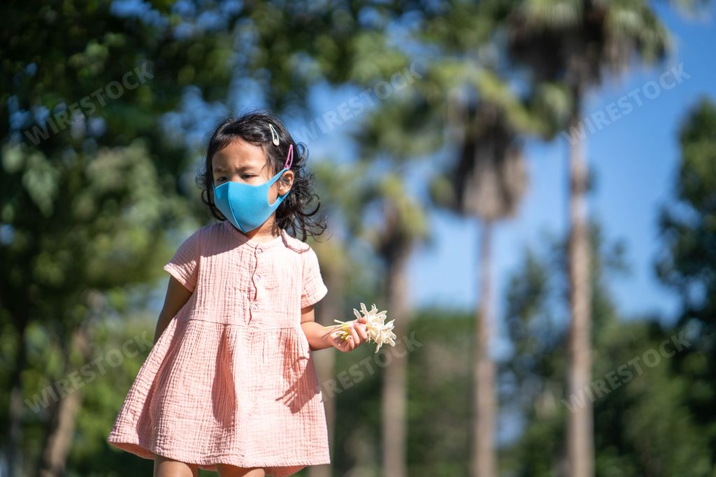 A cute little Thai girl in a protective face mask carrying flowers