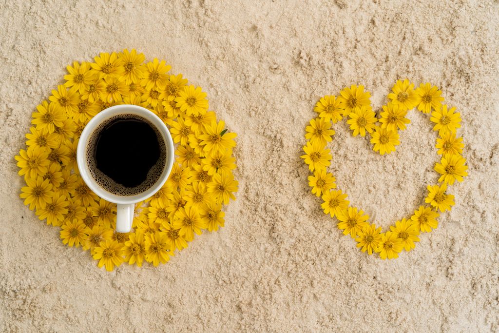 A cup of coffee surrounded by yellow flowers forming a heart on a rock surface