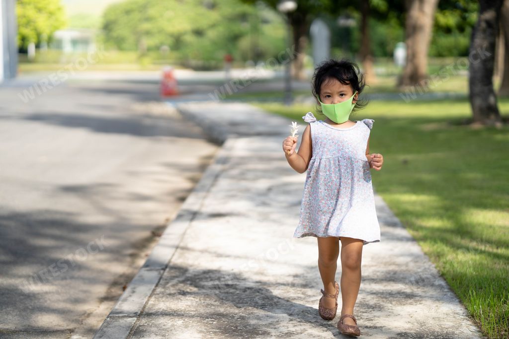 A beautiful Southeast Asian female kid with a mask on her face in the street with flower in her hand