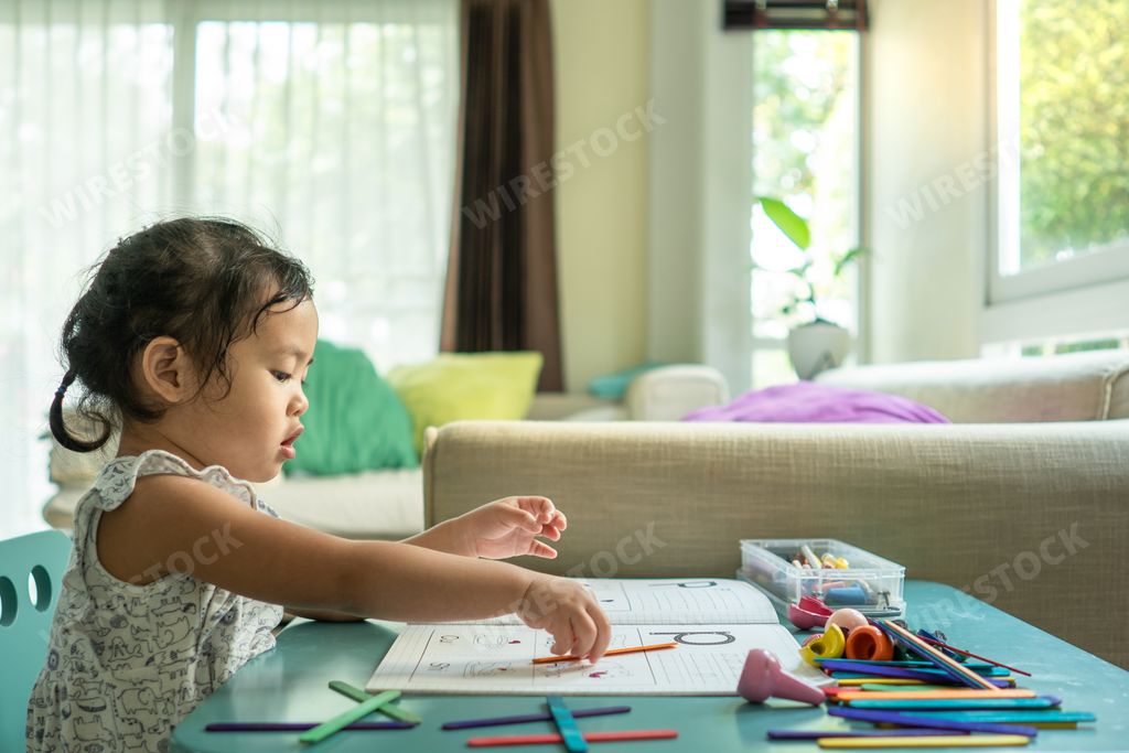 A closeup shot of a Southeast Asian girl learning to read and count at a table indoors