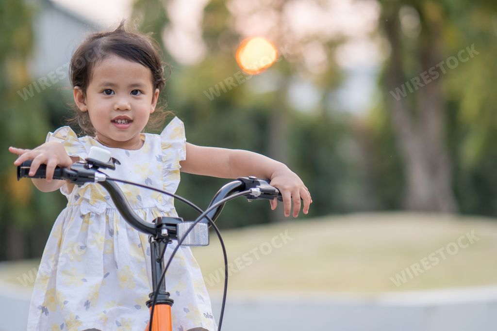 A small Asian female child riding a bike in a park