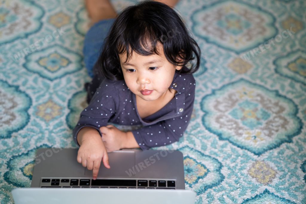 A high angle shot of a cute little Thai girl using a laptop while lying on the floor
