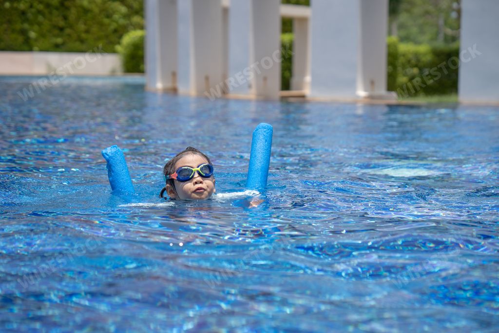 A cute little girl swimming at a pool with goggles and pool noodle