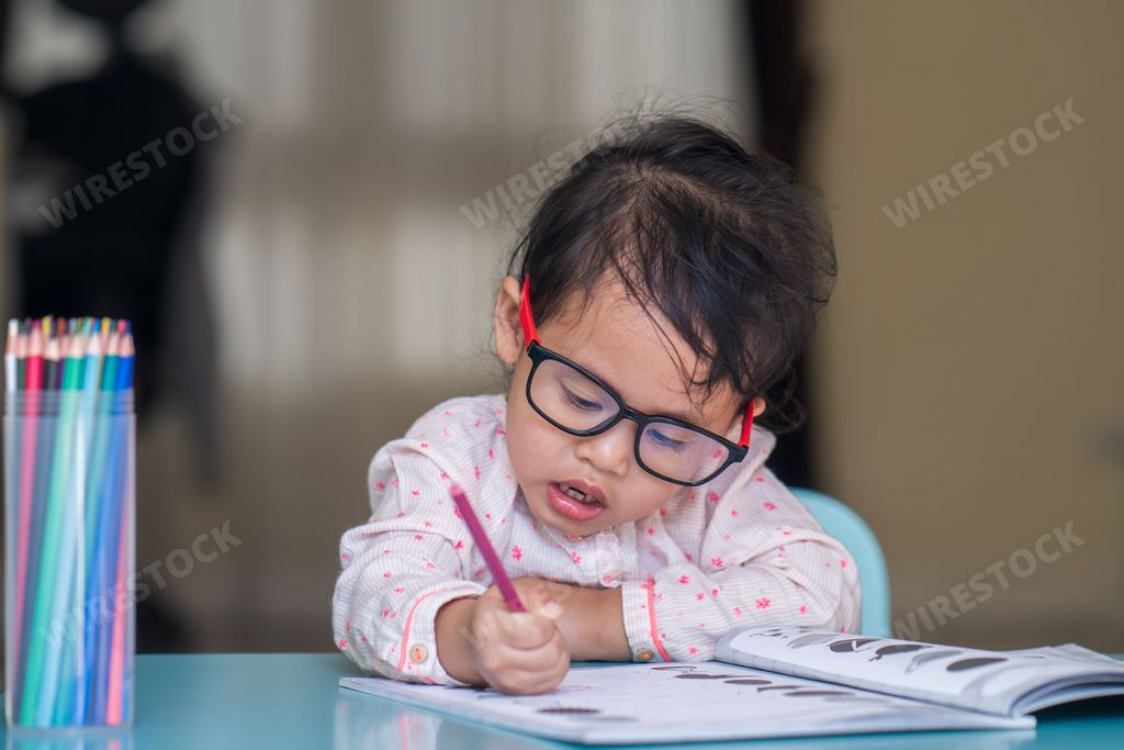 A cute little girl from Thailand in glasses studying indoors