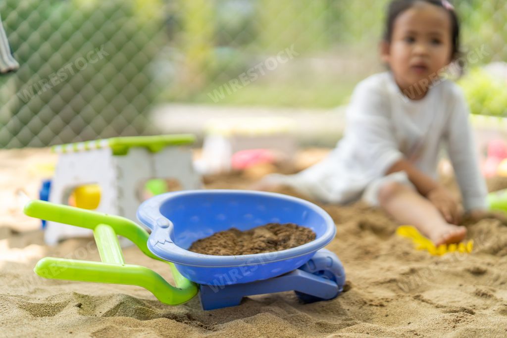 A plastic wheelbarrow toy on a sandpit with a blurred girl background