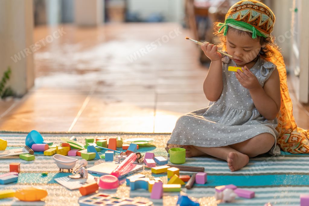 A Thai cute little girl playing wooden building blocks while sitting on a mat