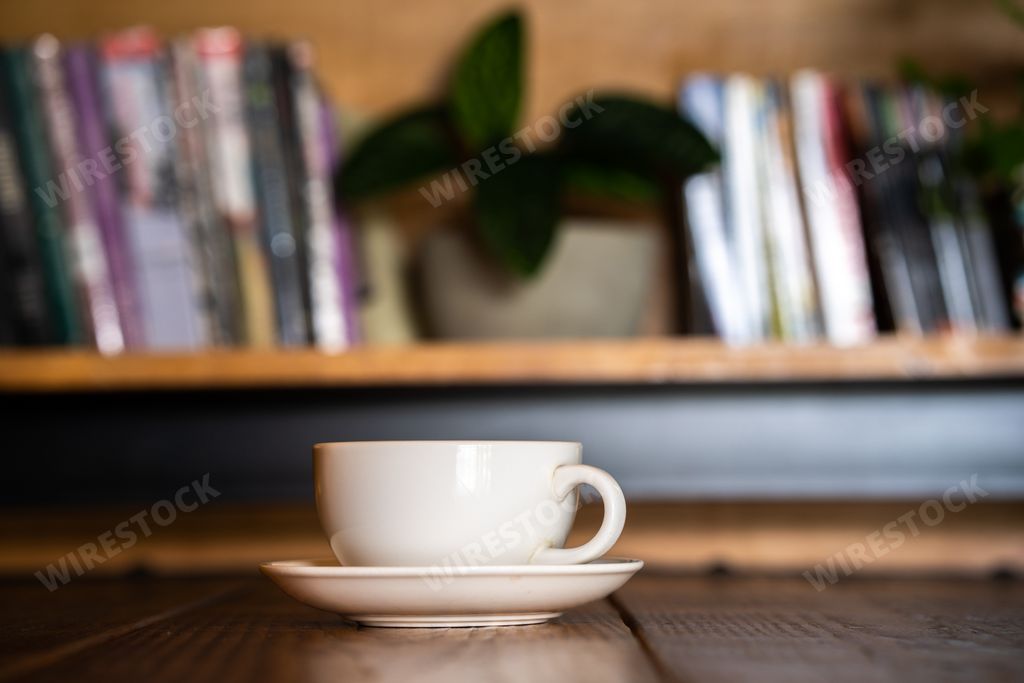 A shallow focus of a beige coffee cup on the table with blurred book shelf in the background