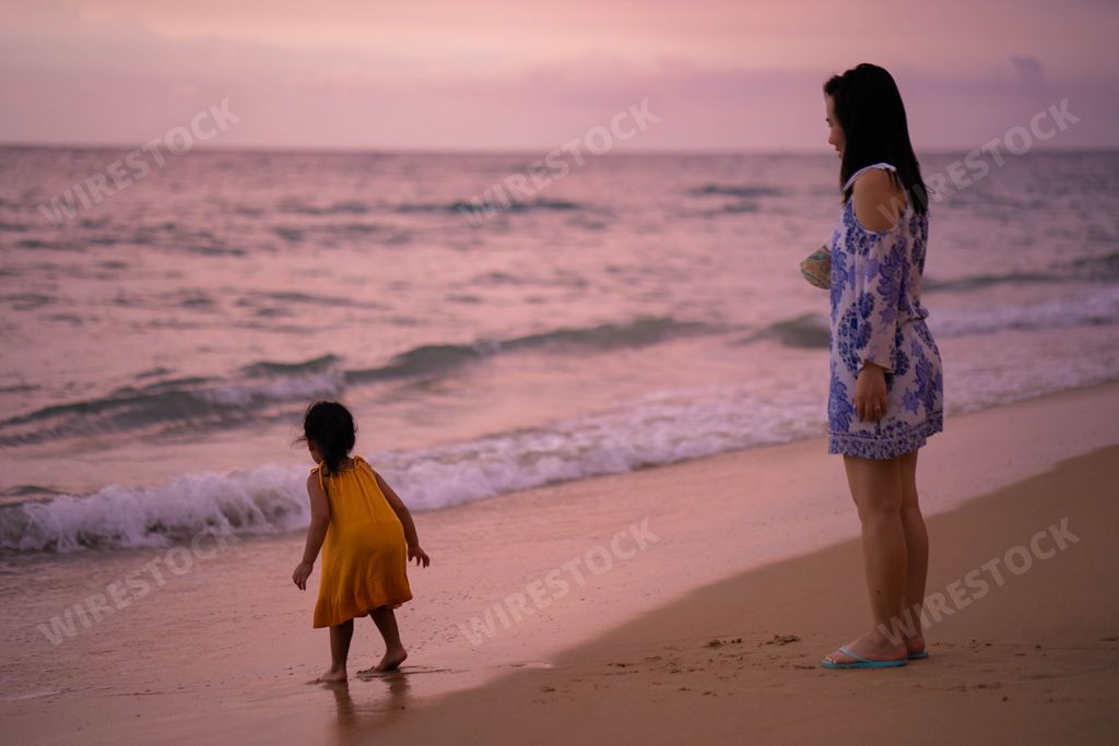 A Southeast Asian mother standing with her little girl in the beach near the water at sunset