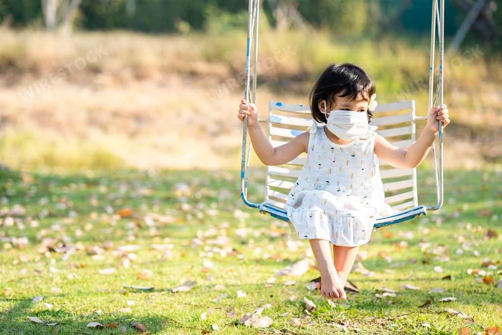 A cute little girl from Thailand in a face mask during the pandemic on the swing having fun