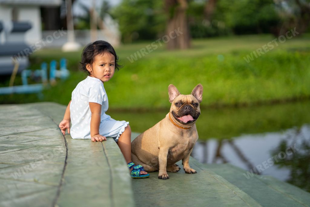 A closeup shot of a Southeast Asian kid with a French bulldog outdoors