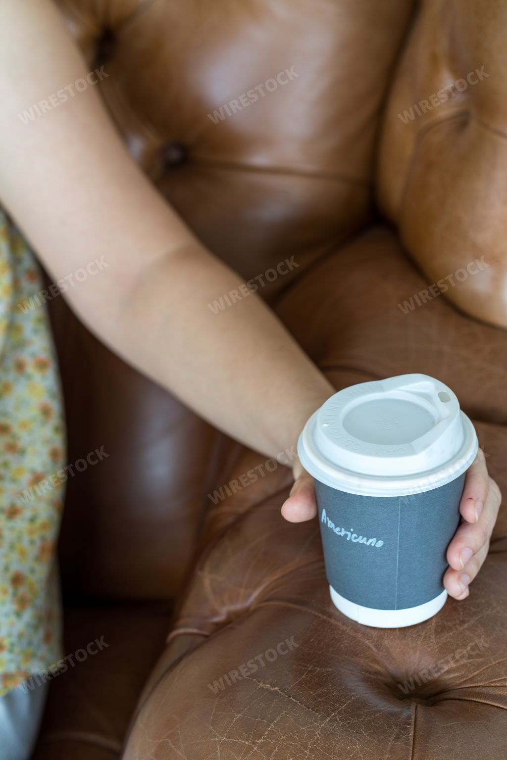 A vertical shot of a female hand holding a paper coffee cup with leather sofa in the background
