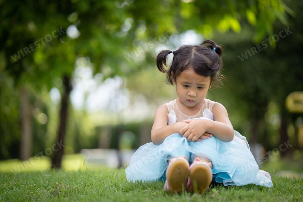 A lonely little Asian girl sitting on green grass in the park