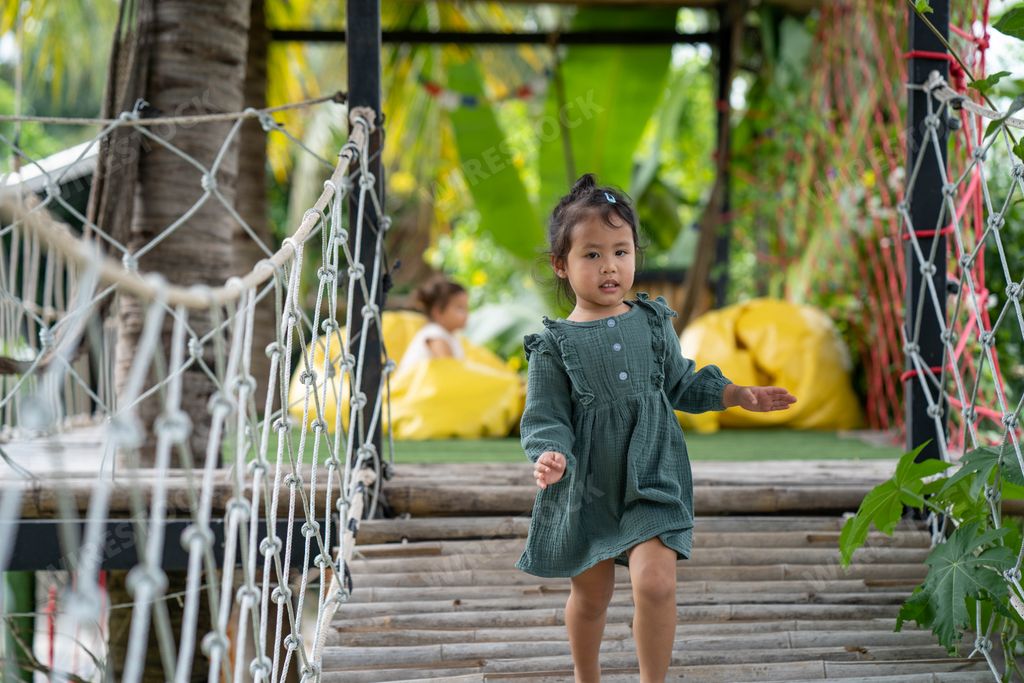 A little girl walking on the bamboo wooden bridge at the playground.