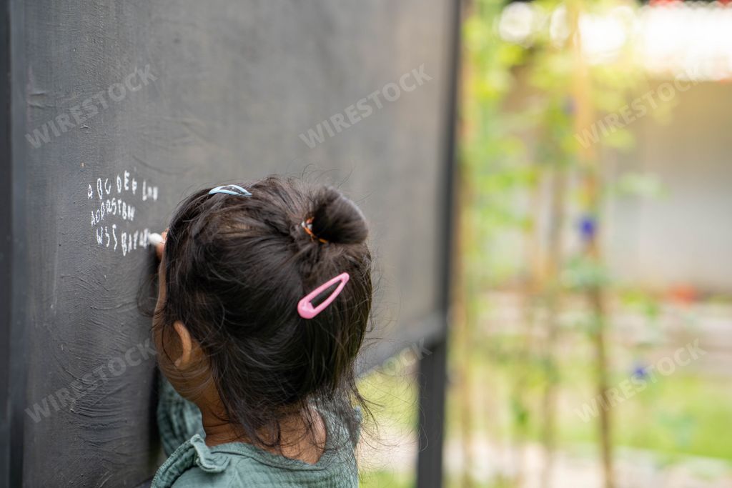 A back view of a cute little Thai girl writing the alphabet on a blackboard
