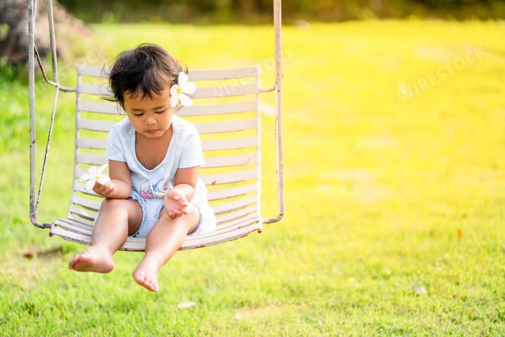 A cute Asian small girl sitting on a swing in a backyard