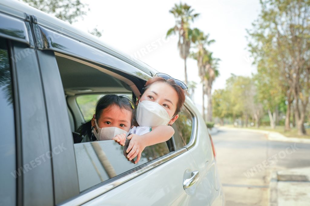 A beautiful Southeast Asian woman and her child wearing face masks looking out of the car window