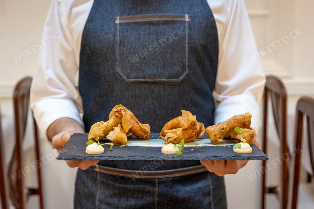 A waiter holding a fancy meal on a black plate in the restaurant