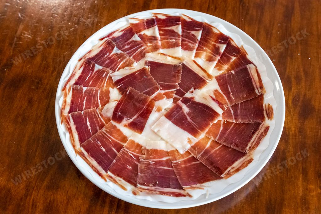 A rustic wooden table with a white plate featuring sliced cured meats