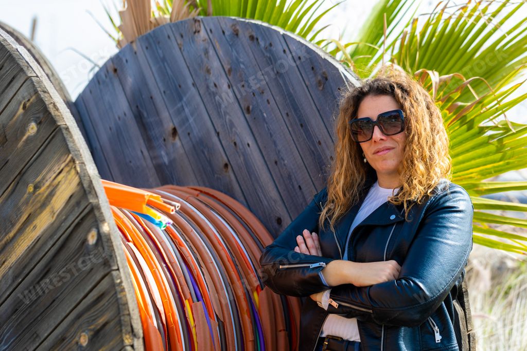 A Caucasian woman with sunglasses posing next to rotated colorful heat shrink tubing wires in the field