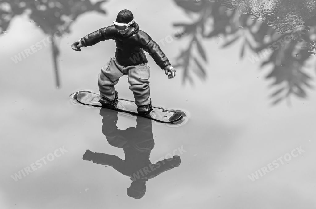A grayscale shot of the reflection of a snowboarder figurine toy in the water