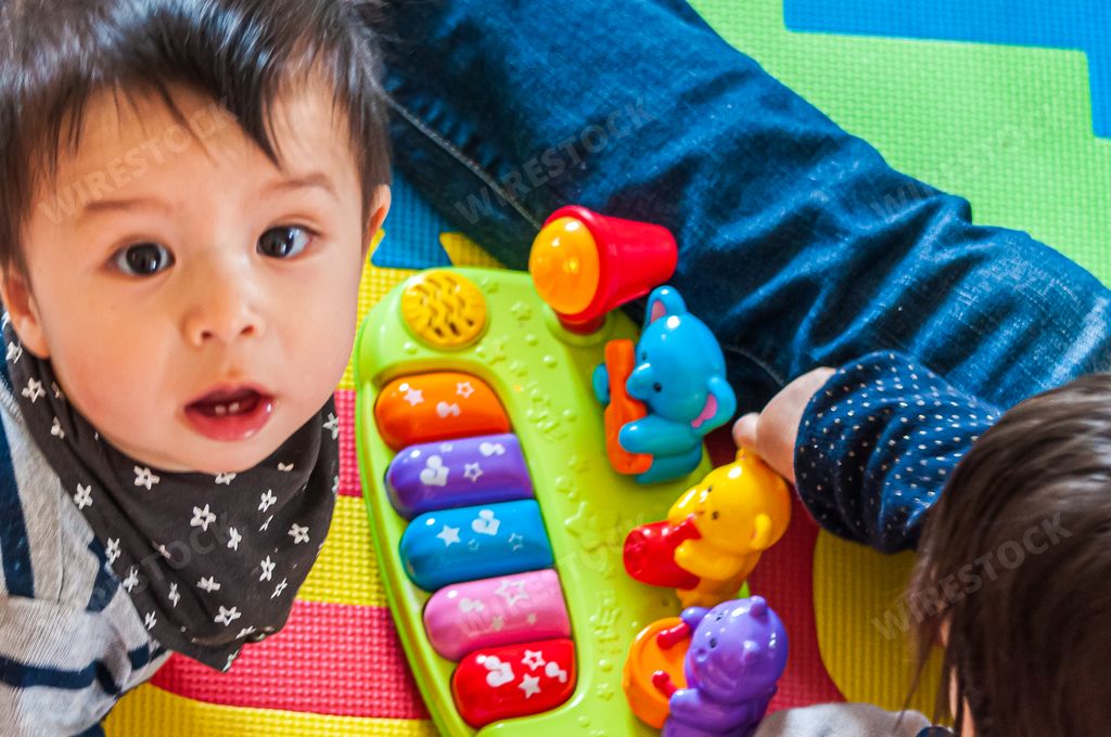 A closeup of a cute Swiss-Thai baby boy staring into the camera with big eyes while his sibling plays beside him with their toys